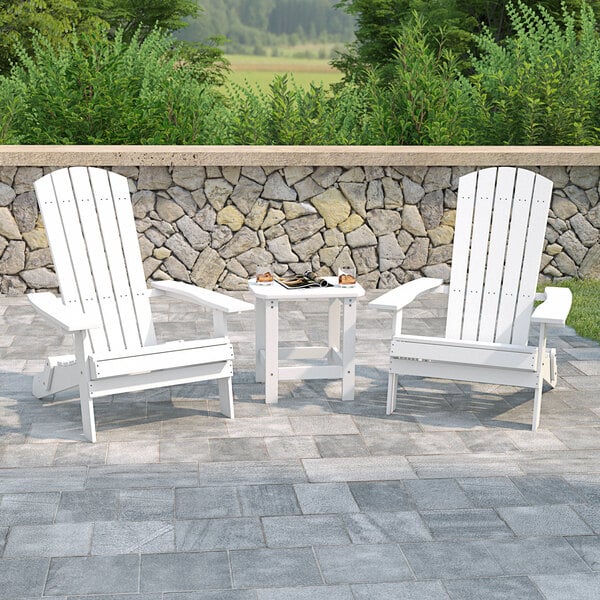 Two white Flash Furniture Charlestown folding Adirondack chairs with a white table on a stone patio.