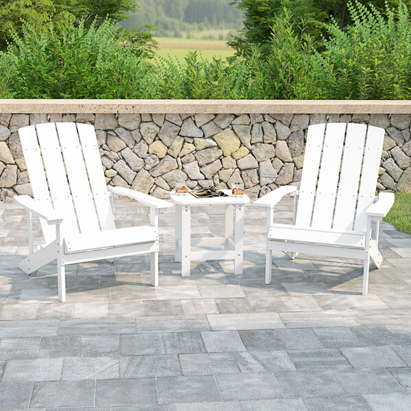 Two white Flash Furniture Adirondack chairs and a table on a stone patio.