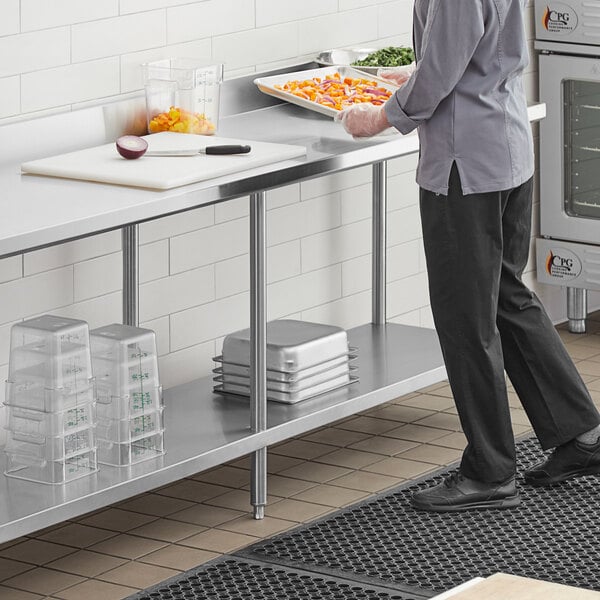 A man in a chef's uniform standing at a Regency stainless steel work table with undershelf.