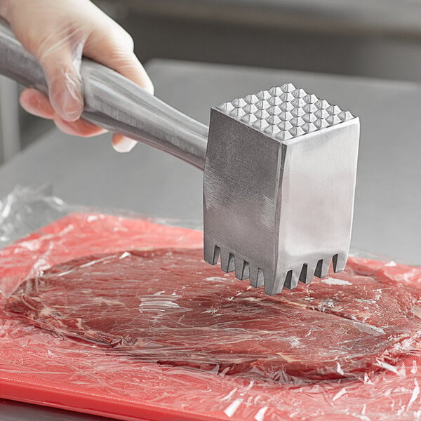 A person using a Choice heavy duty aluminum meat tenderizer on a steak on a counter.