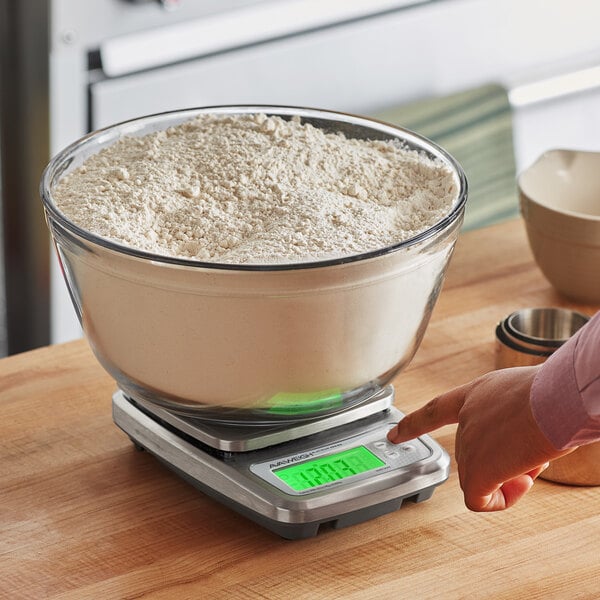 A person using an AvaWeigh digital portion scale to measure flour in a white bowl.