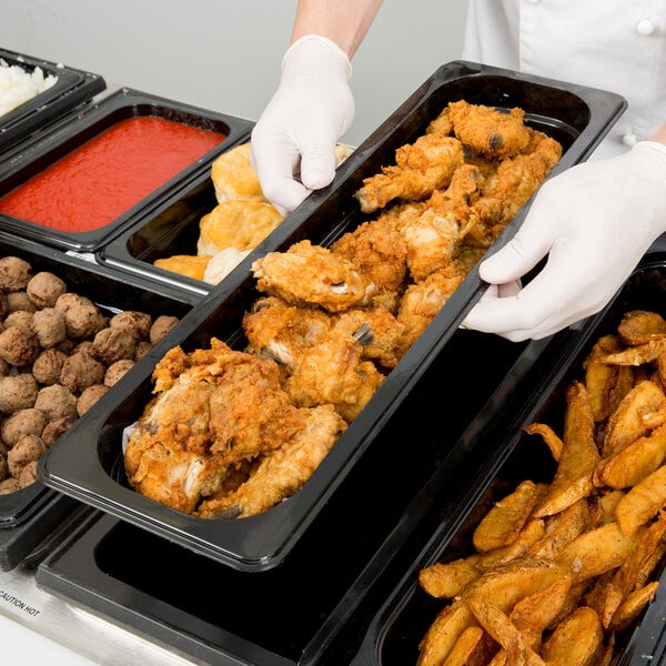 A person in white gloves holding a Cambro black plastic food pan full of fried chicken.