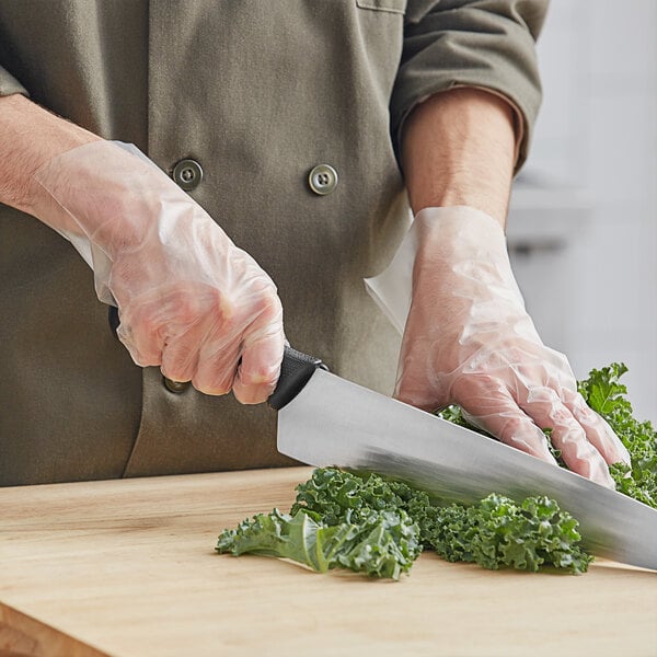 A person cutting kale with Choice disposable gloves on a wooden surface.