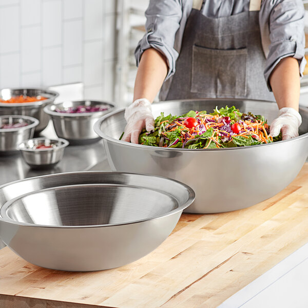 A woman preparing a salad in an extra large stainless steel mixing bowl.
