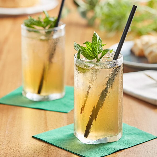 Two glasses of Tractor Beverage Co. Organic Green Tea with black straws and mint leaves on a table.