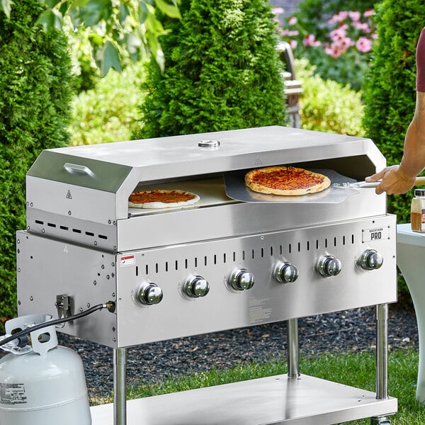 A man using a Backyard Pro pizza oven attachment to cook pizza on a grill.