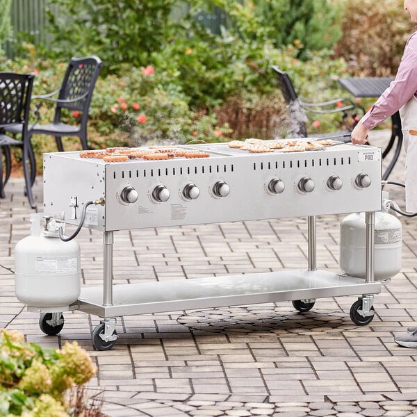A man cooking hot dogs on a Backyard Pro stainless steel outdoor grill on a table in an outdoor setup.