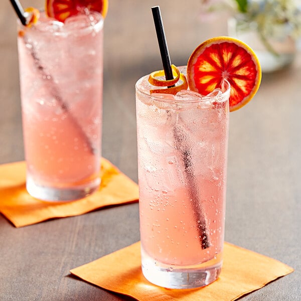 Two glasses of pink Tractor Beverage Co. Organic Blood Orange soda with straws and orange slices.