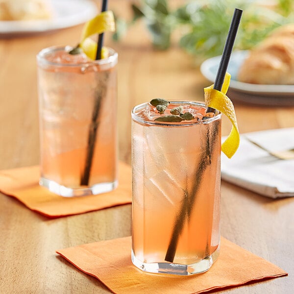 Two glasses of Tractor Beverage Co. Organic Mandarin & Cardamom drinks with straws on a table with lemon wedges.