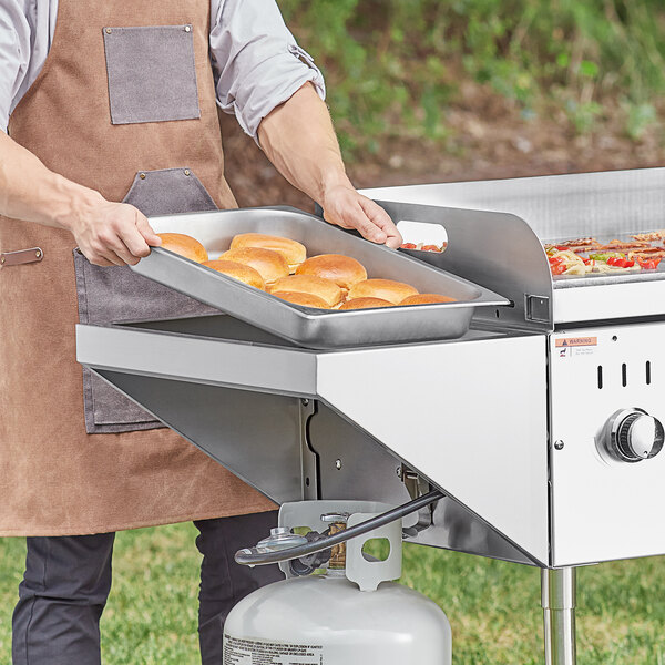 A person cooking food on a Backyard Pro stainless steel end shelf for a grill.
