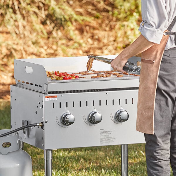 A man using a tool to cook bacon on a Backyard Pro LPG grill.