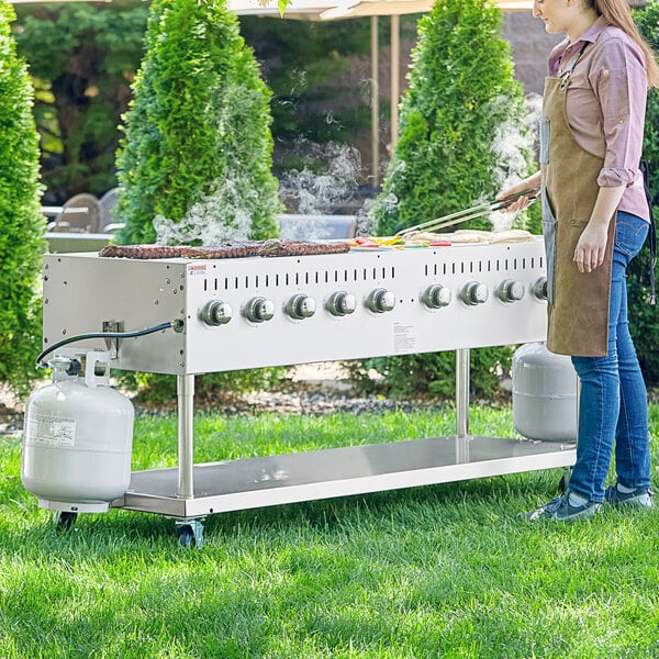 A woman wearing an apron standing next to a Backyard Pro stainless steel outdoor grill.