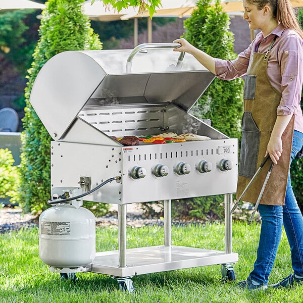 A woman standing next to a 36" stainless steel Backyard Pro outdoor grill.