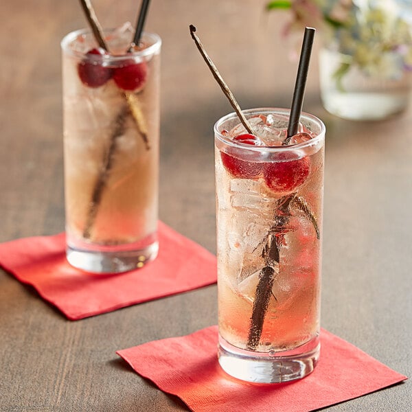 Two glasses of Tractor Beverage Co. cherry soda with straws and cherries on a table.