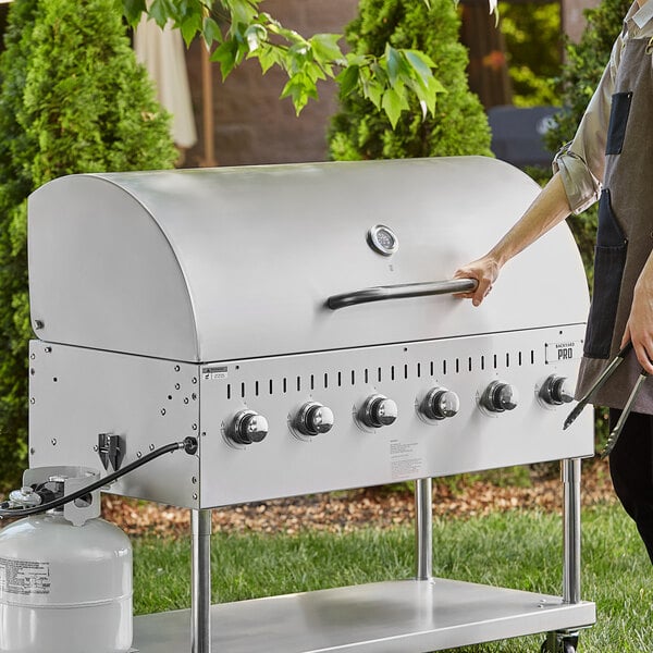 A woman standing next to an LPG48 grill with a Backyard Pro Roll Dome on a counter on an outdoor patio.