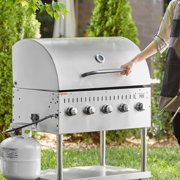A woman standing next to a Backyard Pro grill with a propane tank.