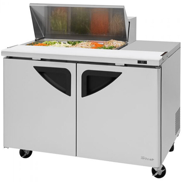 A Turbo Air stainless steel sandwich prep table with glass doors on wheels.