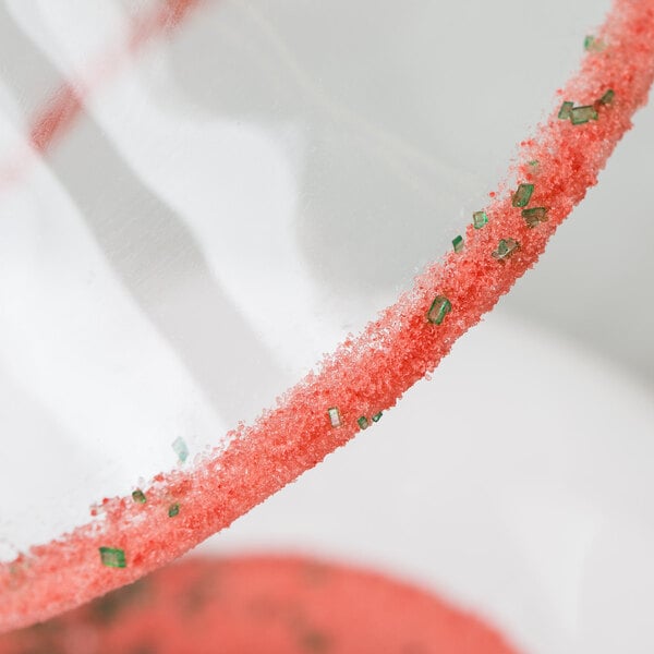 A close-up of a glass with a Rokz watermelon cocktail rim with red and green sugar.