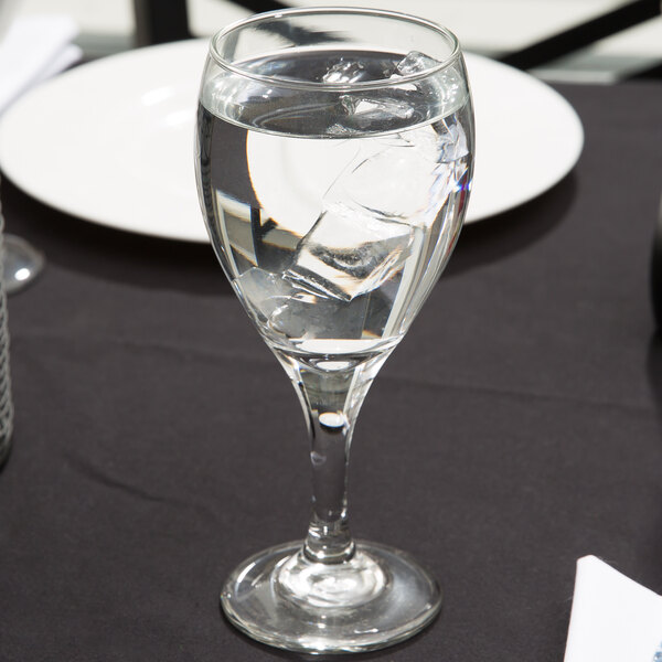 A Libbey Teardrop goblet filled with ice water on a table with a plate and silverware.