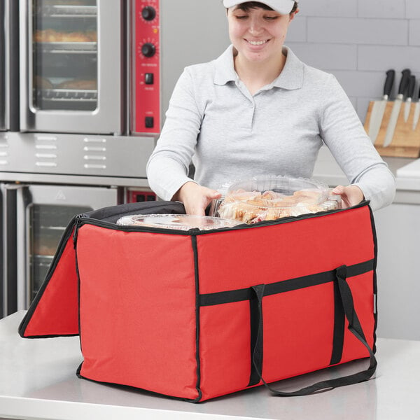A woman in a white cap holding a red Choice insulated food delivery bag with food inside.