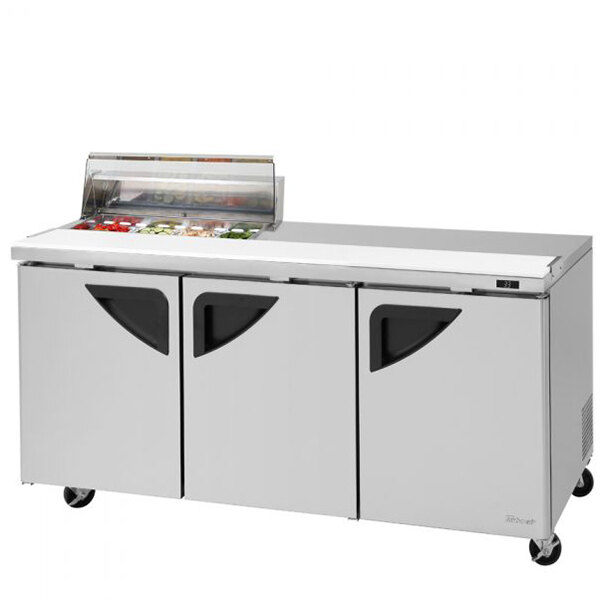 A Turbo Air stainless steel refrigerated sandwich prep table with clear lids over three trays.