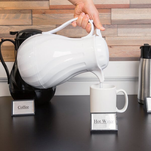 A person pouring coffee from a white Choice thermal coffee carafe into a mug.
