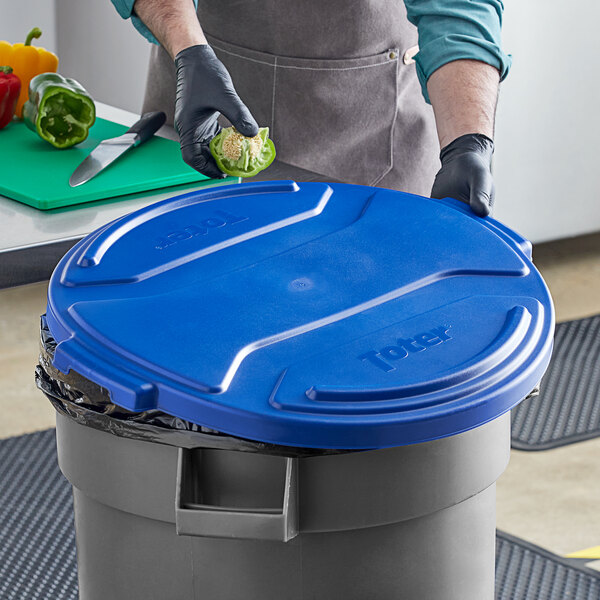 A man in blue gloves putting food into a blue Toter lid on a trash can.