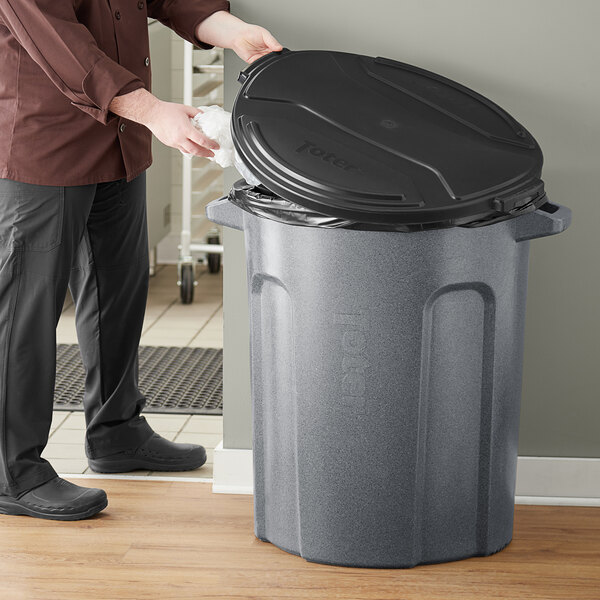 A man opening a Toter dark gray trash can with a black lid.