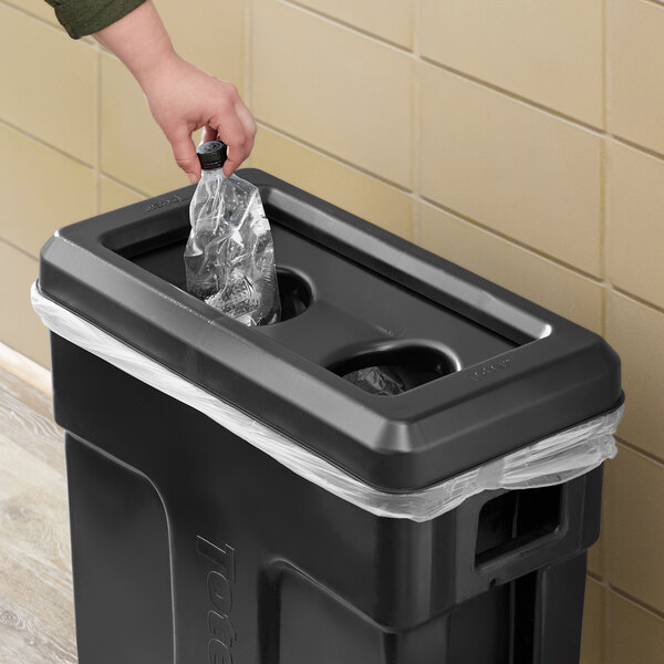 A person putting a Toter Black Bottle / Can Lid on a black trash can full of plastic bottles.