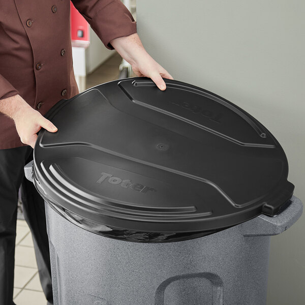A man in a chef's jacket placing a black Toter lid on a trash can.