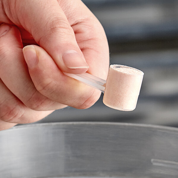 A hand holding a 2.5 cc polypropylene scoop over a white surface.