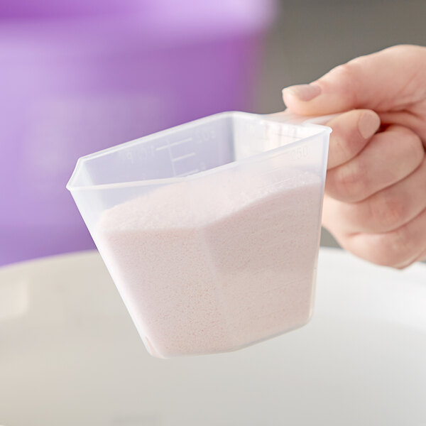 A hand holding a Polypropylene Measuring Cup filled with a white substance.