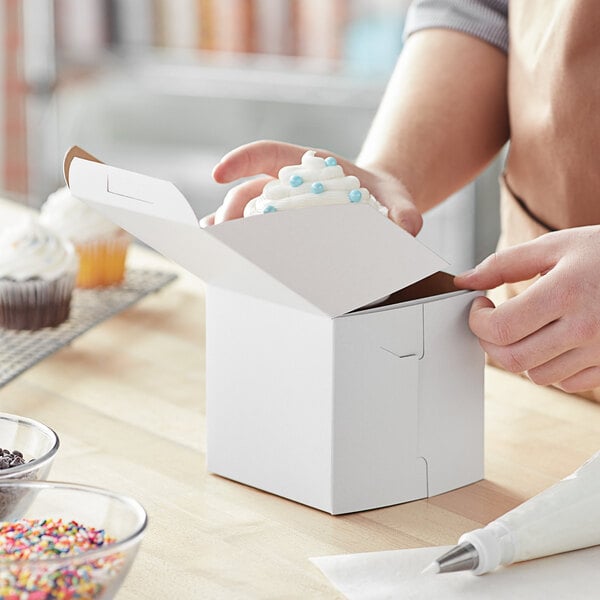 A person's hand holding a cupcake in a white Baker's Mark box.