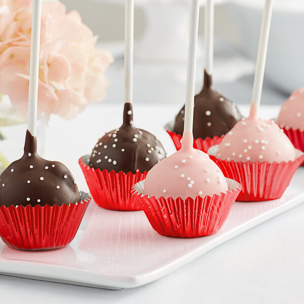 A group of chocolate cake pops in Enjay red foil wrappers on a white plate.