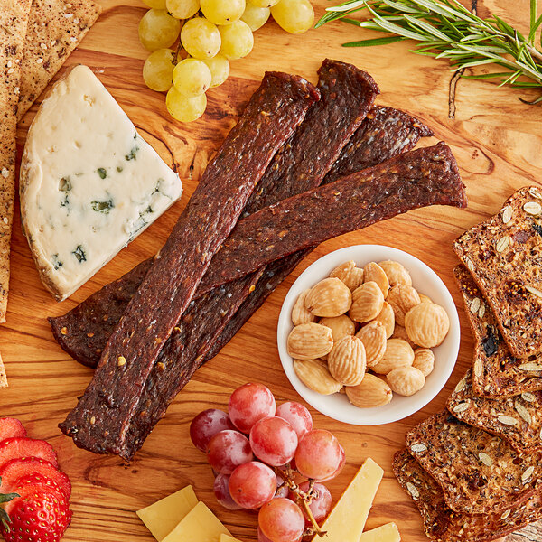 A wood table with a variety of snacks including cheese, fruit, and Shaffer Venison Farms Hot Venison Jerky.