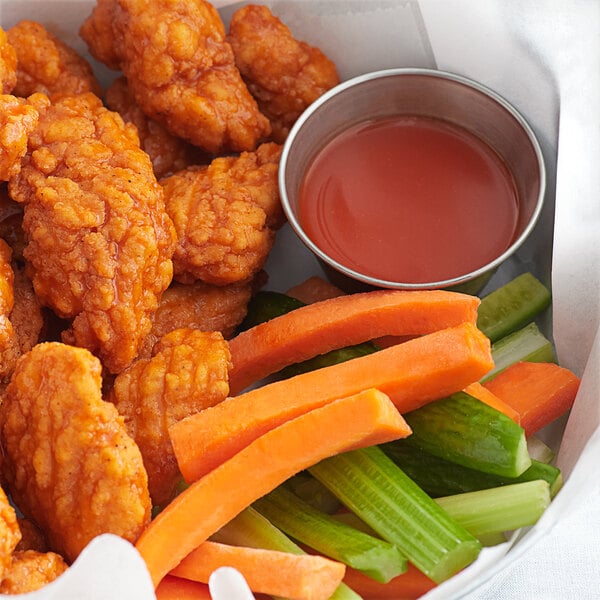 A plate of chicken wings with carrots and celery dipped in Crystal hot sauce.