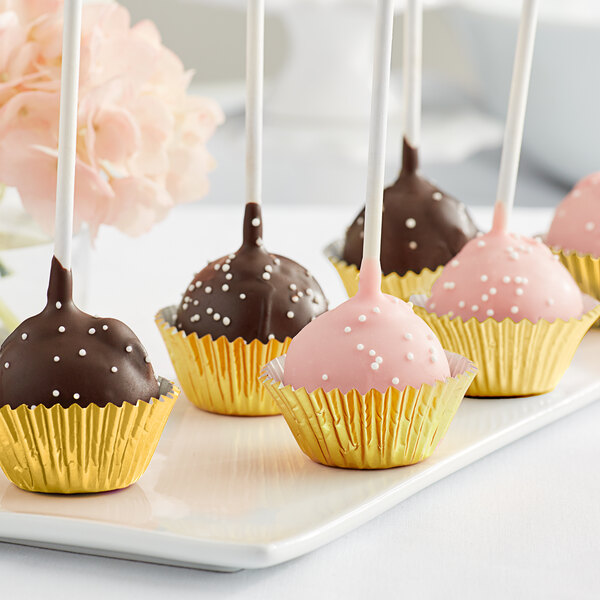 A group of chocolate covered cake pops in gold foil mini baking cups on a white plate.