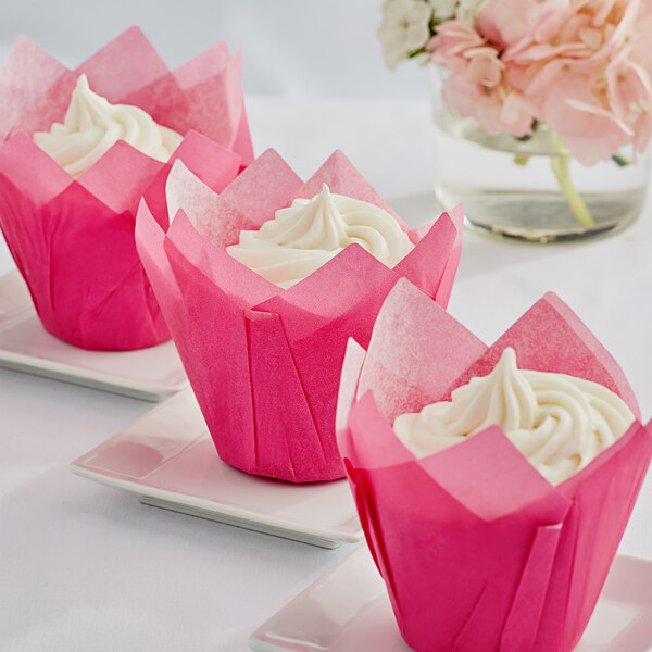 Three pink tulip cupcakes on white plates with white frosting.