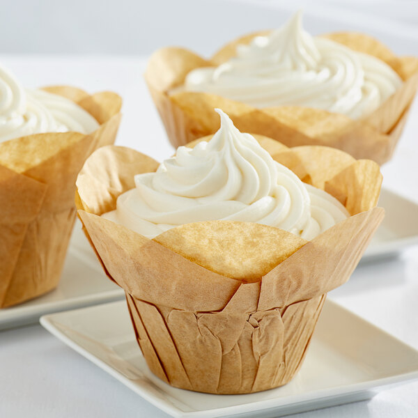 Three Enjay lotus brown baking cups with white frosting on top of cupcakes.