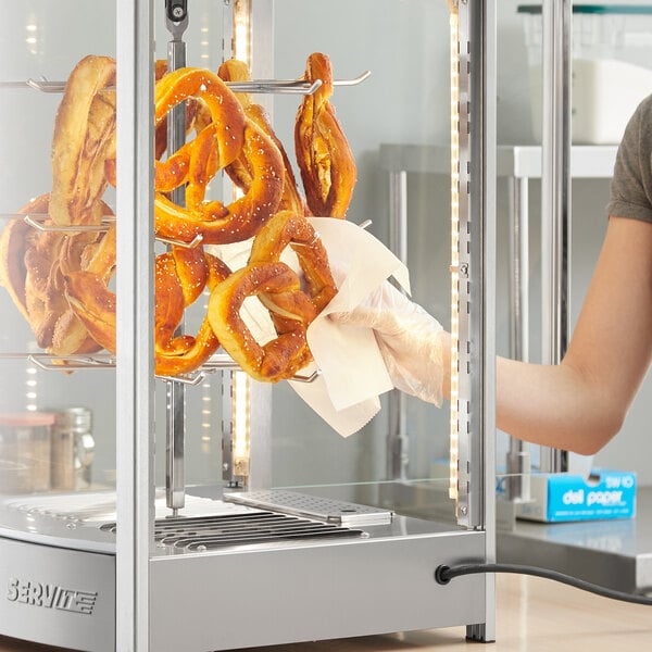 A woman using a ServIt pretzel rack to display pretzels in a glass case.