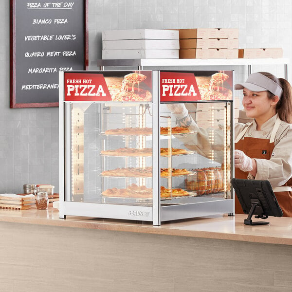 A woman wearing a brown apron and gloves using a ServIt pizza warmer to display pizzas.