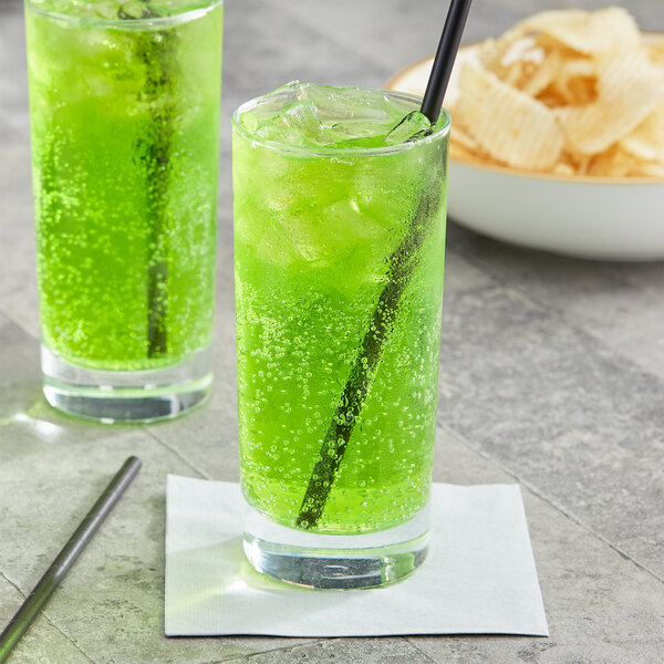 Two glasses of Jones Green Apple soda with straws on a table with chips.