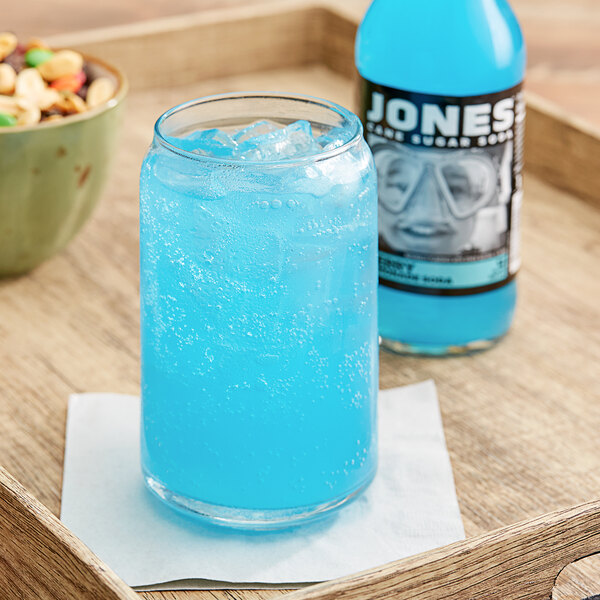 A close-up of a Jones Berry Lemonade Soda in a glass on a table next to a bowl of food.