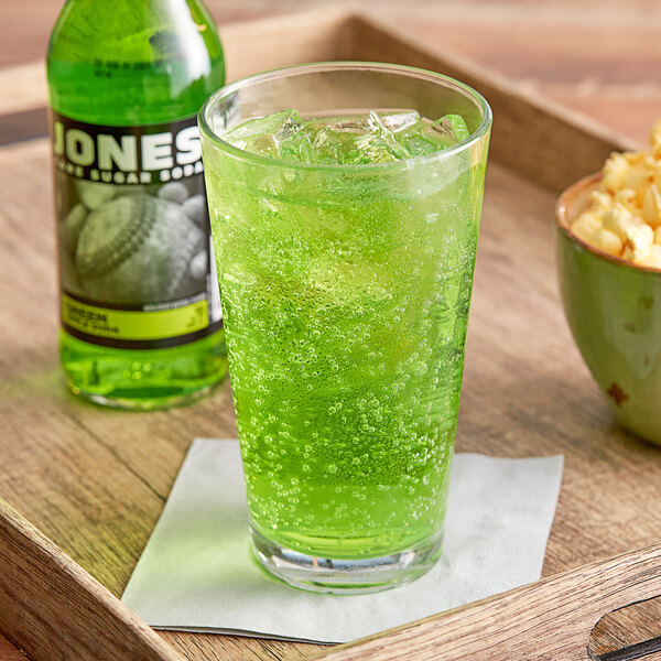 A glass of Jones Green Apple Soda on a tray with a bottle of popcorn.