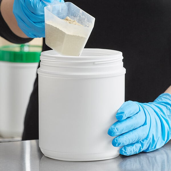 A person in blue gloves pouring white powder into a white HDPE plastic canister.