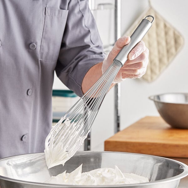 A person using a Choice 16" stainless steel piano whisk to mix white food in a bowl.