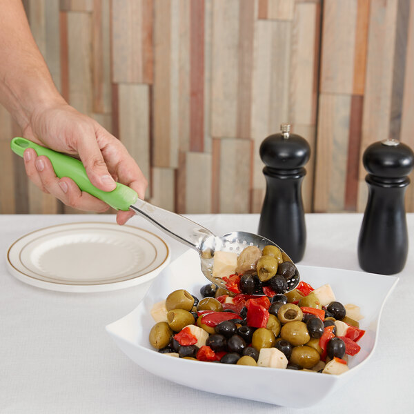 A person using a Vollrath Jacob's Pride 14" Heavy-Duty Perforated Basting Spoon with a green Ergo Grip handle to serve olives.
