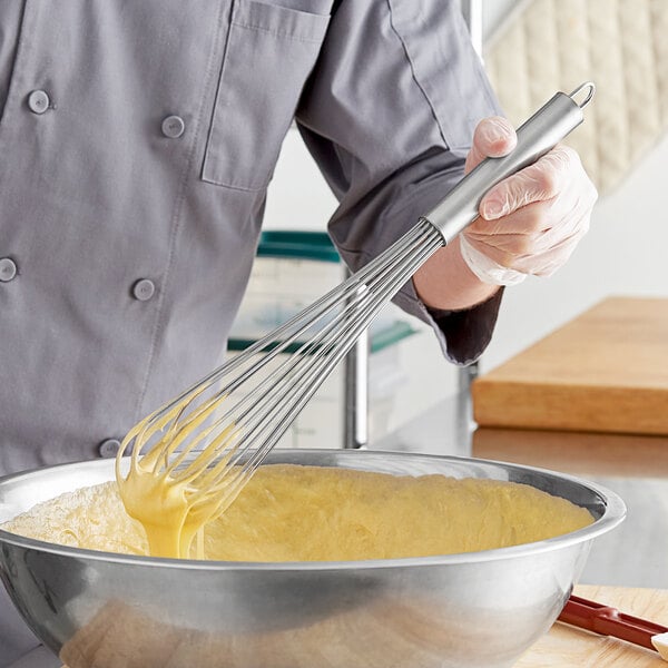 A person using a Choice 16" Stainless Steel French Whisk to mix batter in a bowl.