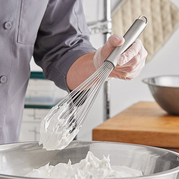 A person mixing whipped cream in a bowl with a Choice stainless steel whisk.