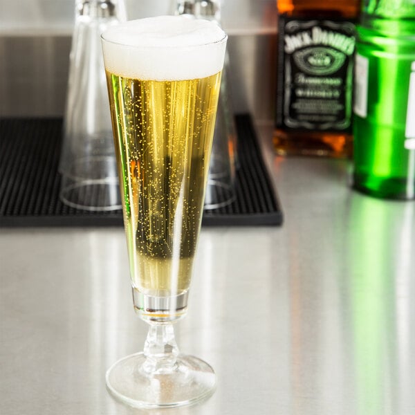A Libbey footed pilsner glass filled with beer on a counter.